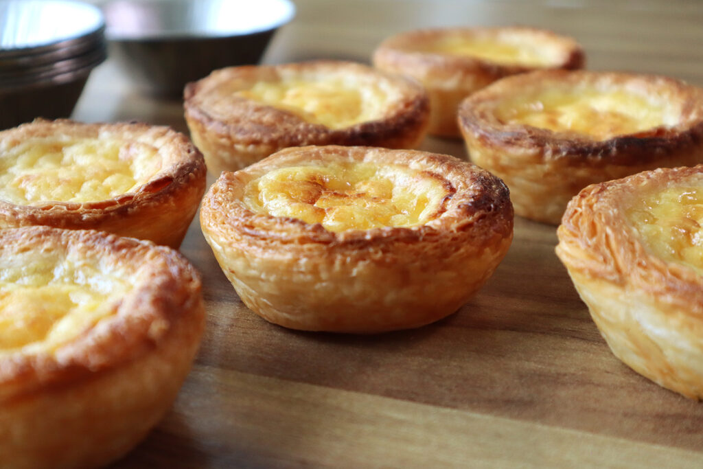 Pastéis de Nata servidos numa mesa de Thanksgiving, com uma massa folhada estaladiça e recheio cremoso, polvilhados com canela, trazendo um toque clássico e doce da tradição portuguesa à celebração.